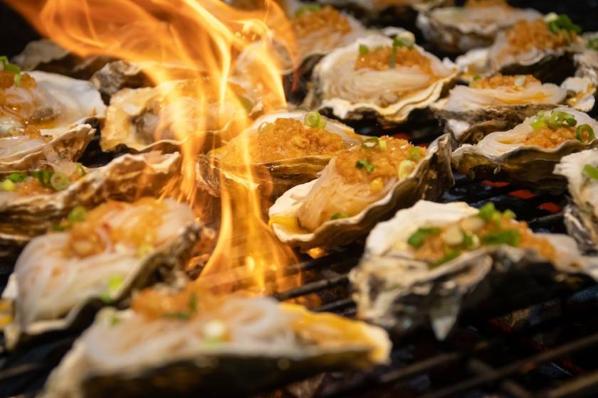 Grilled oyster with garlic butter, scallion and crispy topping on hot flame, savory seafood grill delight, smoky aroma and sizzling presentation.