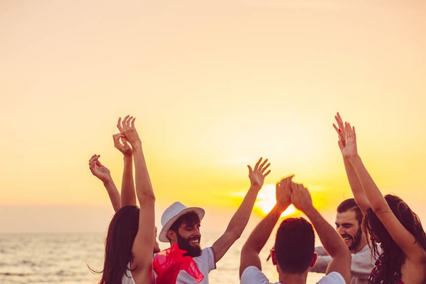 People dancing at the beach with hands up.